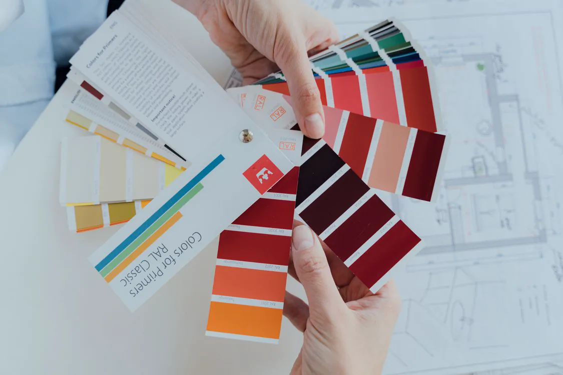 Hands reviewing paint color swatches over a floor plan