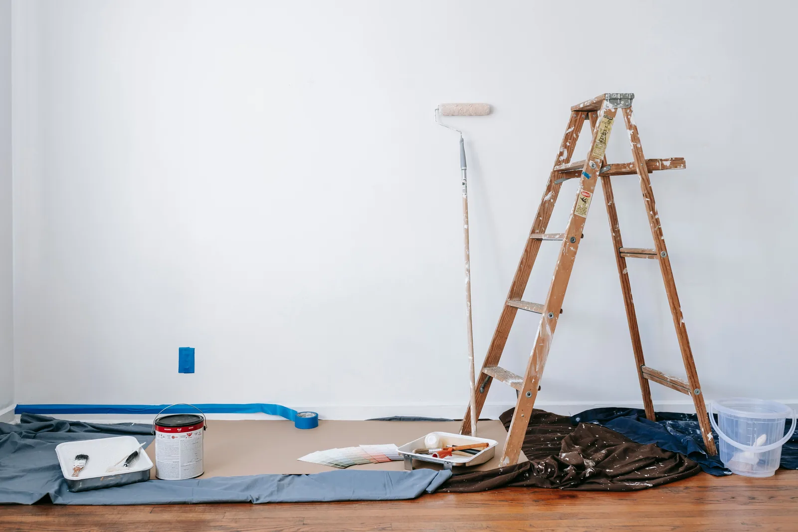 Empty office interior prepared with a ladder, roller, drop cloth, and paint supplies