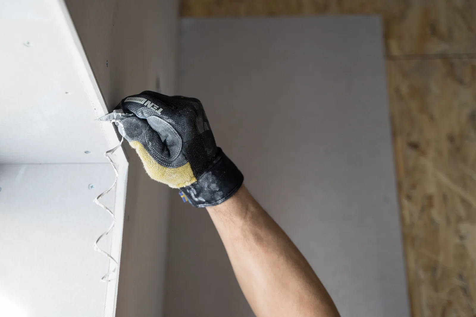 Gloved hand applying joint compound to a drywall edge
