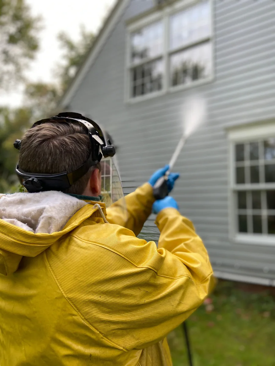 Worker power washing the siding of a house