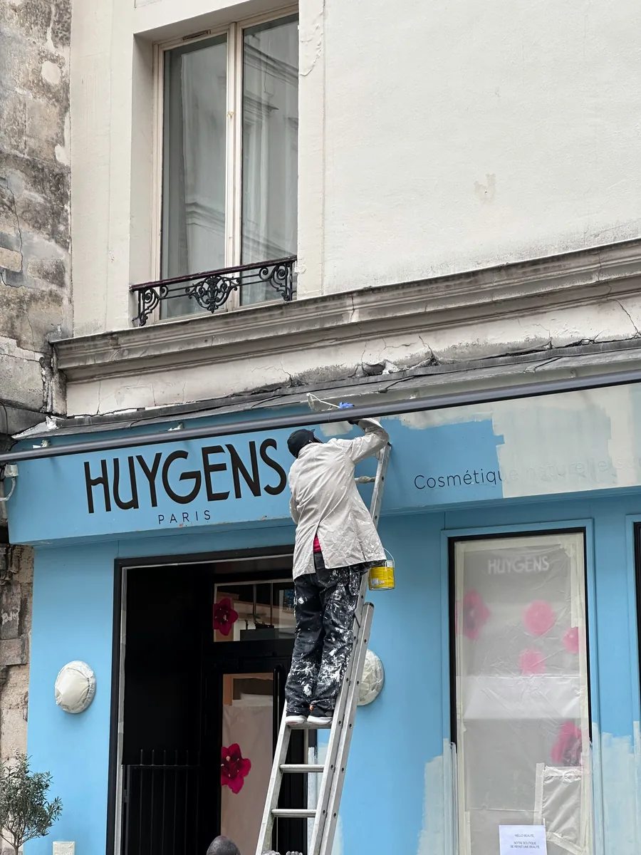 Painter working from a ladder on a blue storefront exterior