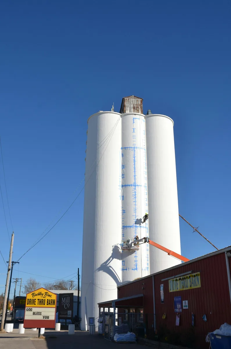 Workers coating a tall white industrial silo
