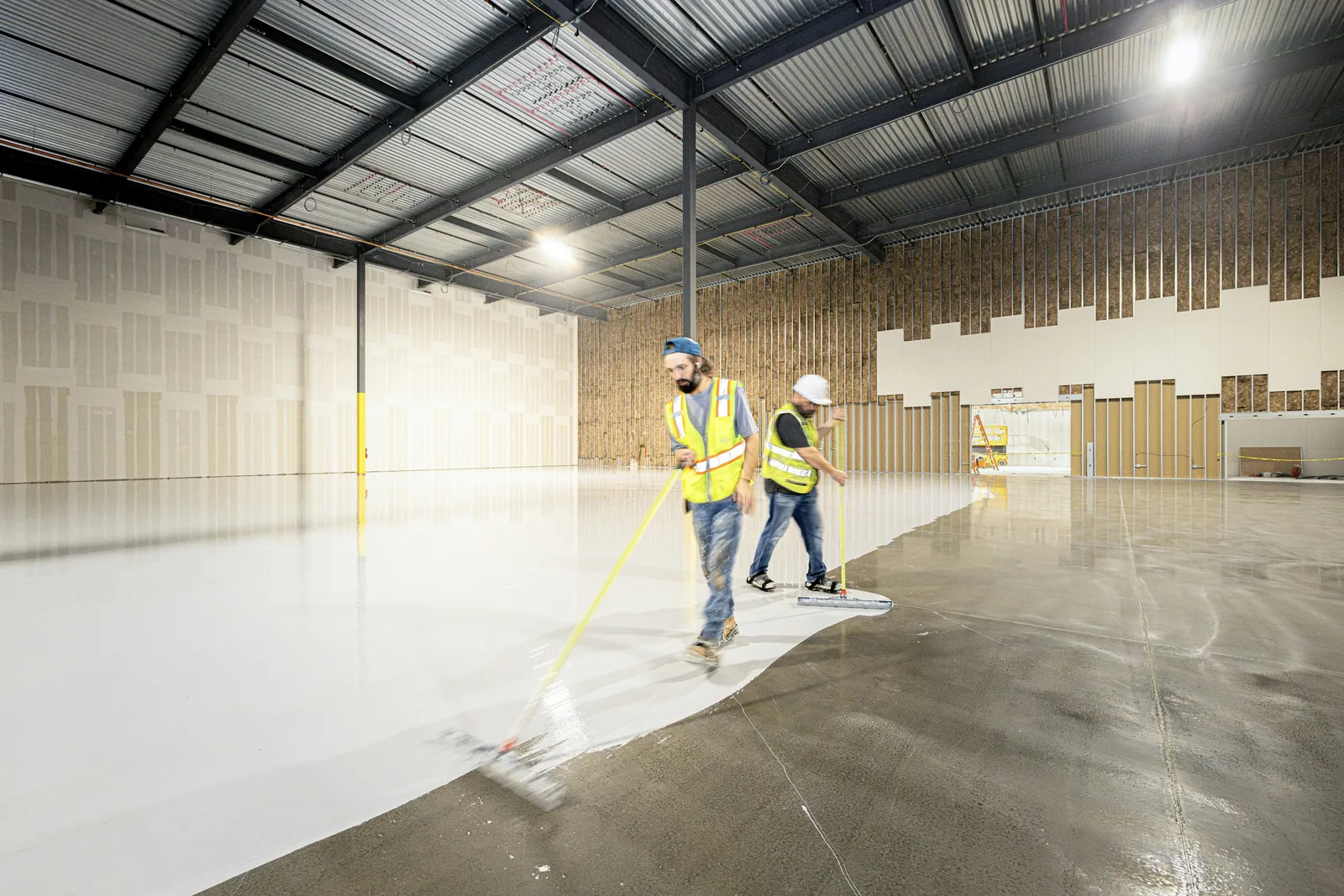 Workers coating the floor of a large empty warehouse